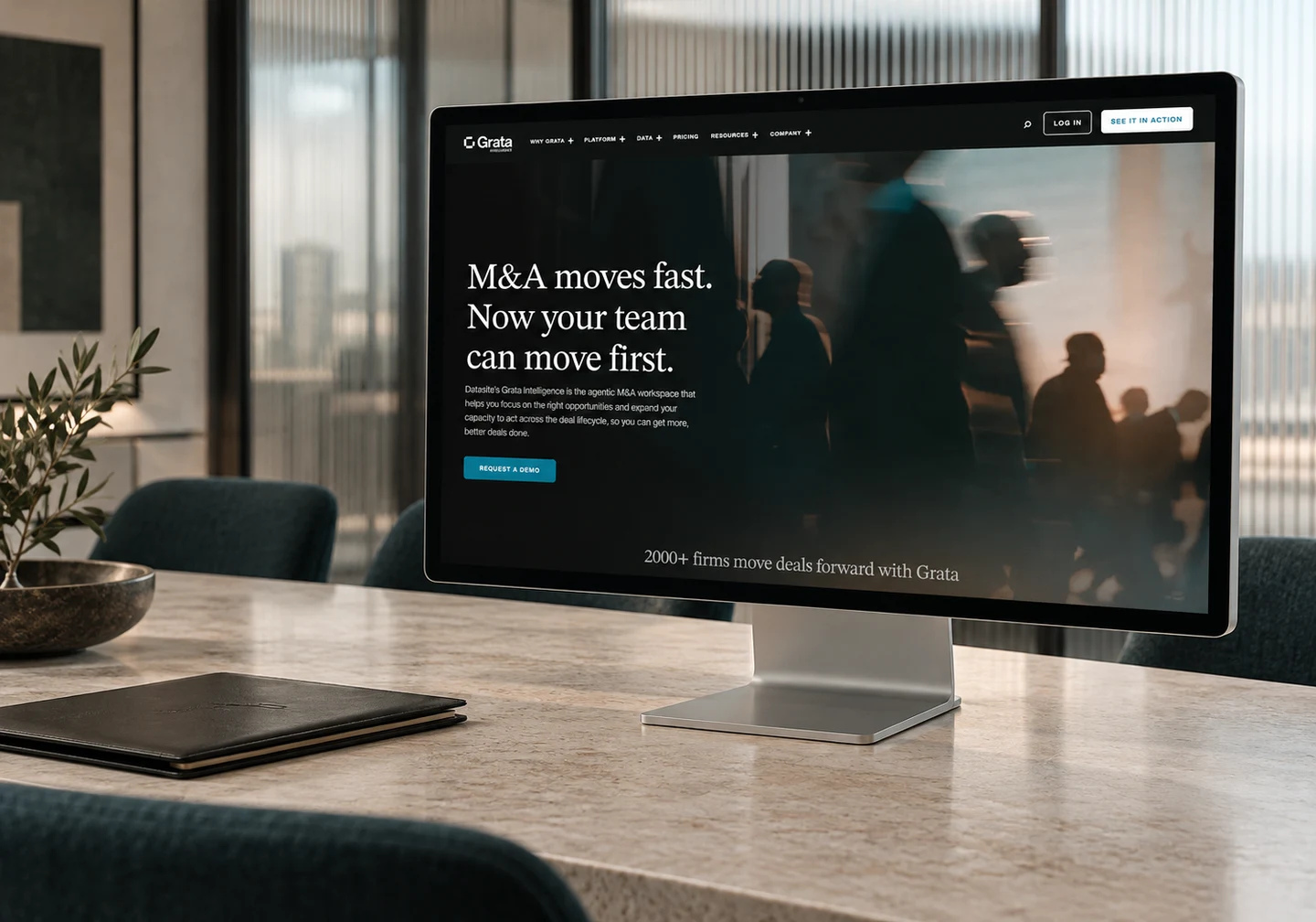 Grata Intelligence homepage on an Apple Studio Display in a contemporary meeting room.